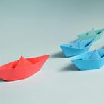 Colorful origami paper boats arranged to depict leadership and teamwork concepts.