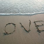 Love written in sand with ocean waves at the beach, evoking romance and tranquility.