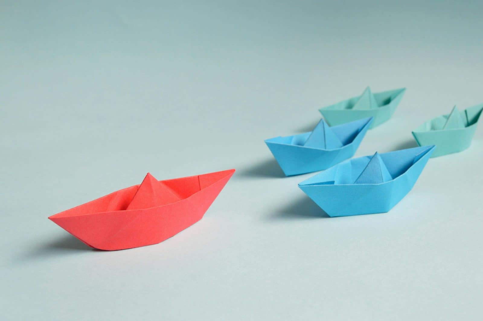 Colorful origami paper boats arranged to depict leadership and teamwork concepts.