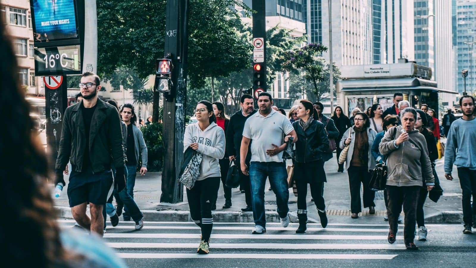 A diverse group of people crossing a street in a bustling city setting with skyscrapers.